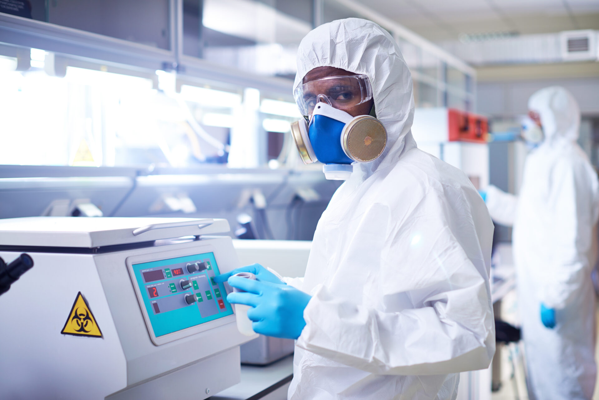 Scientist in lab coat operating centrifuge.