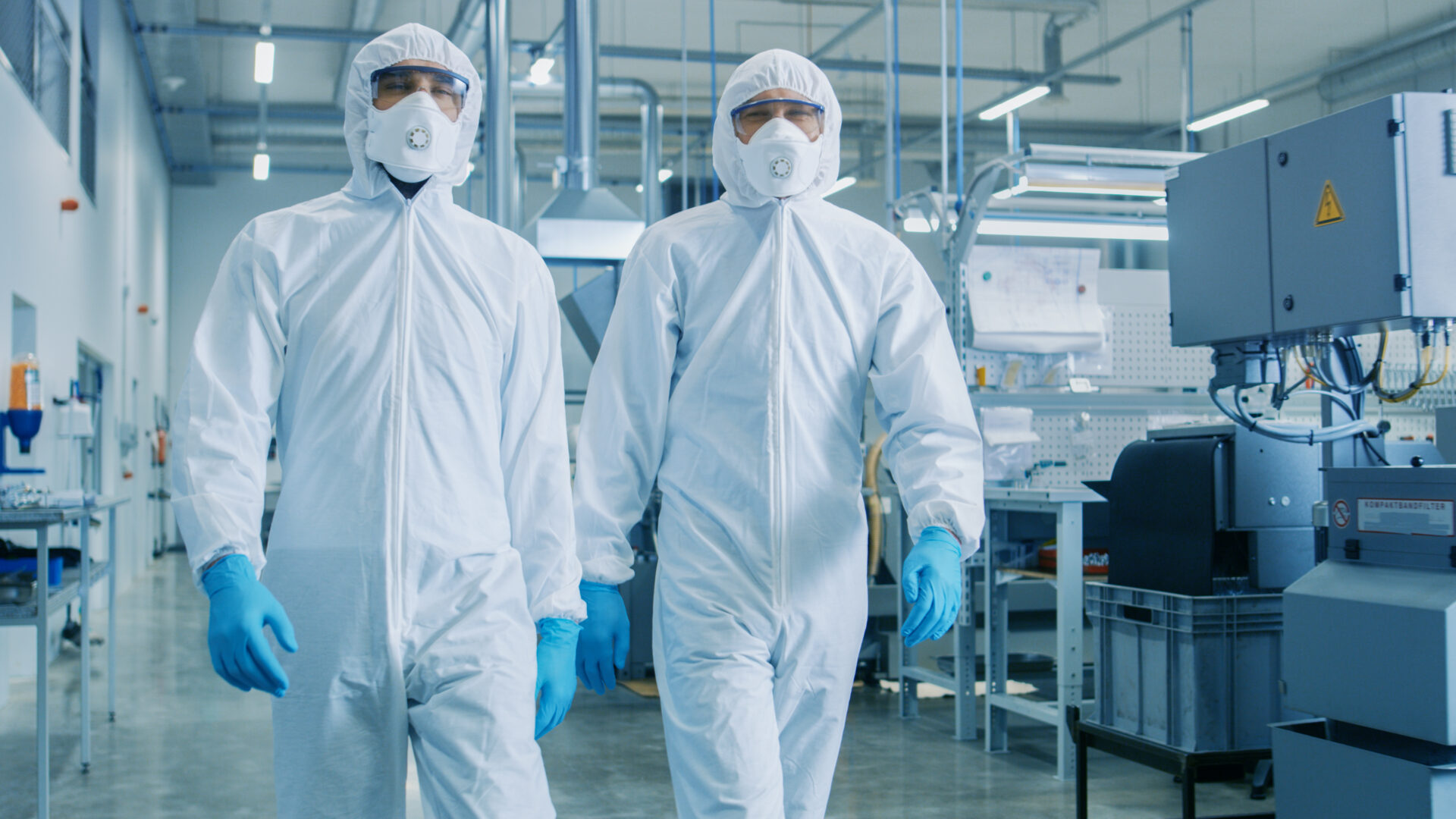 Two workers in clean suits walk through factory.